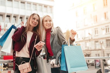 Şehirde alışveriş yaptıktan sonra akıllı telefon kullanan mutlu kız arkadaşlar.