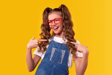 Gözlüklü ve kot pantolonlu neşeli liseli kız kendini gösteriyor.