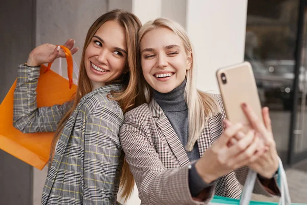 Neşeli şık kız arkadaşlar alışveriş yaparken selfie çekiyorlar.