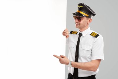 Erkek pilot boş bir posteri işaret ediyor.