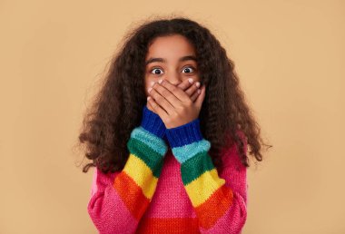 Şaşırmış etnik kız elleriyle ağzını kapatıyor.