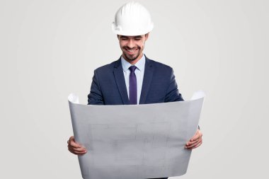 Kask takmış gülümseyen mimar planlarını okuyor.