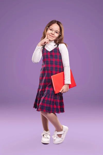 Slimme schoolmeisje in uniform en bril met boek — Stockfoto
