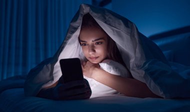 Genç kadın yatakta akıllı telefon kullanıyor.