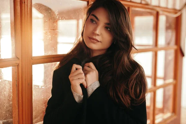 Dreamy woman in warm coat standing near window — Stock Photo, Image