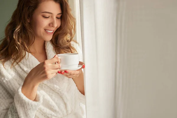 Mujer joven bebiendo café cerca de la ventana — Foto de Stock