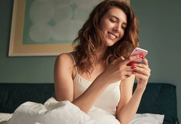 Boldog nő használja okostelefon ébredés után — Stock Fotó