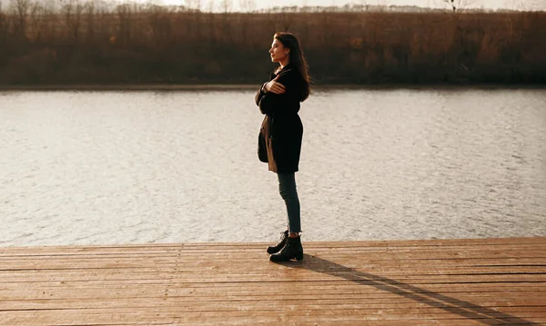 Wanita yang tenang berdiri di dermaga dekat danau saat matahari terbenam — Stok Foto