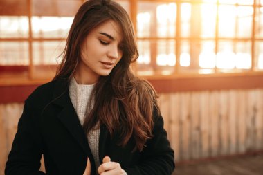 Gün batımında terasta duran ceketli sakin kadın.