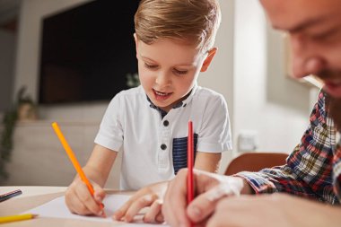 Baba ve oğul evde birlikte resim çiziyorlar.
