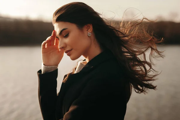 Mujer soñadora de pie cerca del lago al atardecer —  Fotos de Stock