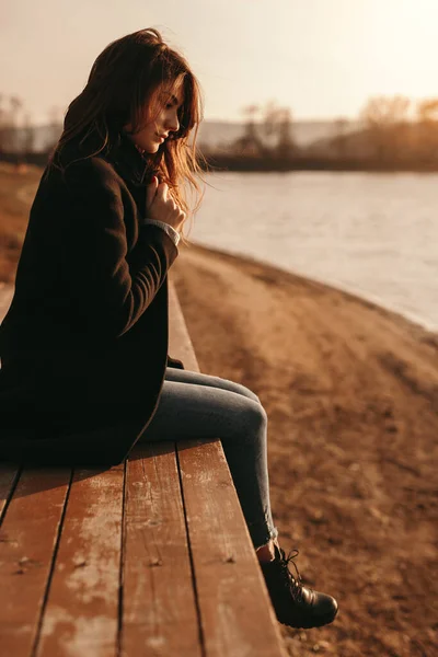 Gün batımında göl kenarındaki iskelede oturan huzurlu kadın. — Stok fotoğraf