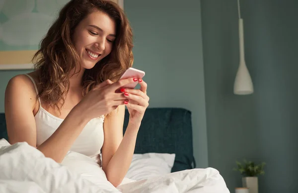 Donna felice messaggistica su smartphone a letto — Foto Stock
