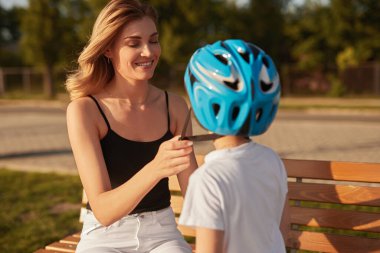 Anne parkta oğluna miğfer takıyor.