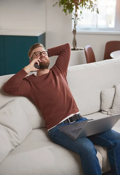 Pozytywny mężczyzna freelancer mówi na smartfonie na kanapie — Zdjęcie stockowe