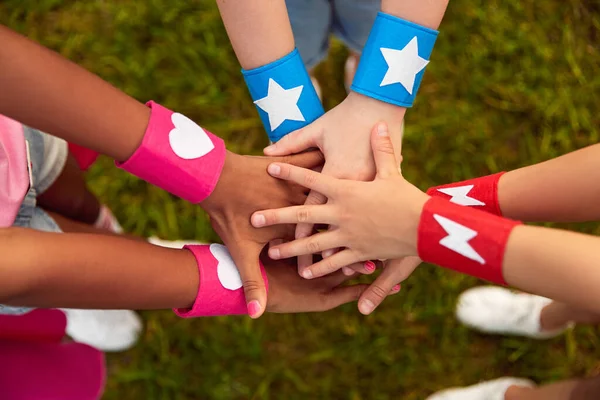 Diversos niños con pulseras de superhéroes apilando manos —  Fotos de Stock