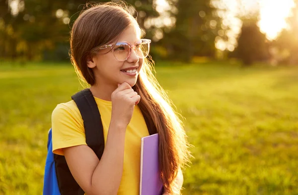Весела школярка в окулярах, стоячи в парку — стокове фото