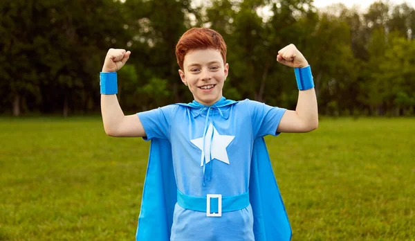 Cheerful superhero kid showing muscles in nature — 图库照片