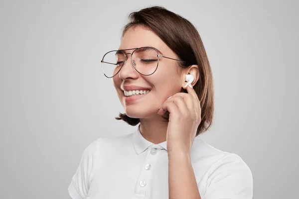 Cheerful young woman adjusting TWS earphones — Stock Fotó
