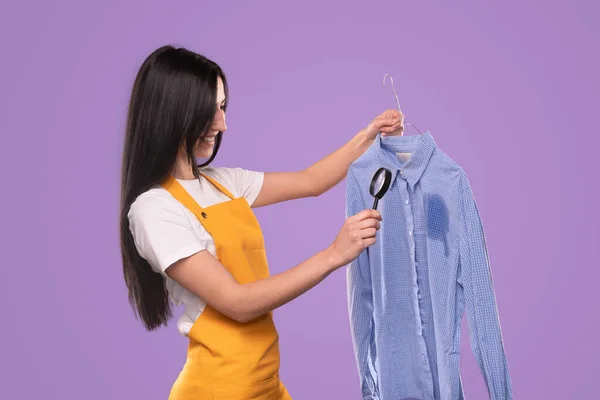 Woman with magnifier looking at stain on shirt — Stock Fotó