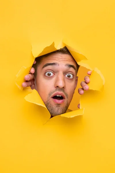 Shocked guy peeking from hole in paper — Stock Photo, Image