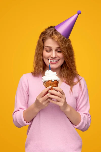 Mujer contenta en sombrero de fiesta haciendo deseo con cupcake de cumpleaños —  Fotos de Stock