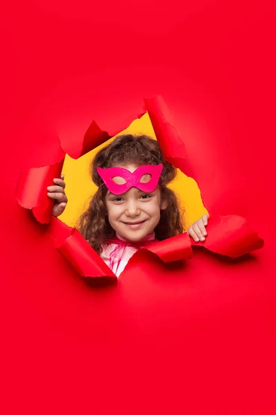 Chica sonriente con máscara rosa mirando a través del agujero en el papel — Foto de Stock