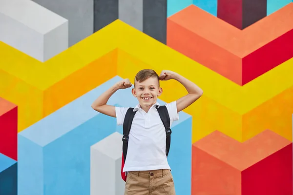 Веселий школяр, що показує м'язи на барвистій стіні — стокове фото