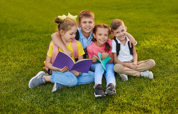 Happy schoolkids with copybooks sitting on grass — Stock Photo, Image