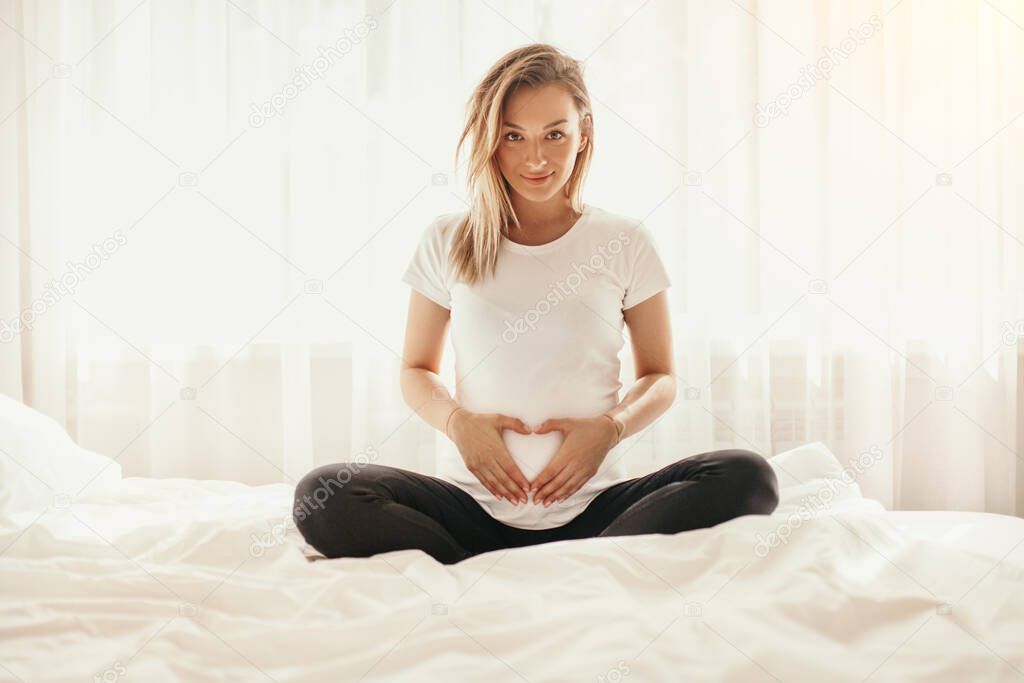 Happy pregnant woman sitting on bed