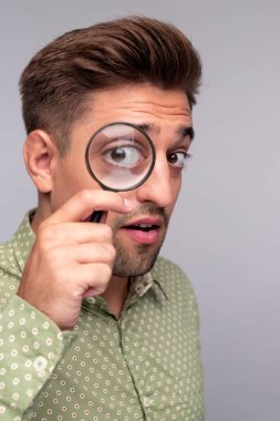 Büyüteci olan meraklı bir adam kameraya bakıyor.