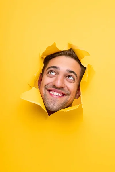 Αστείος χαμογελαστός άντρας κοιτάζει μέσα από την τρύπα στο κίτρινο χαρτί — Φωτογραφία Αρχείου