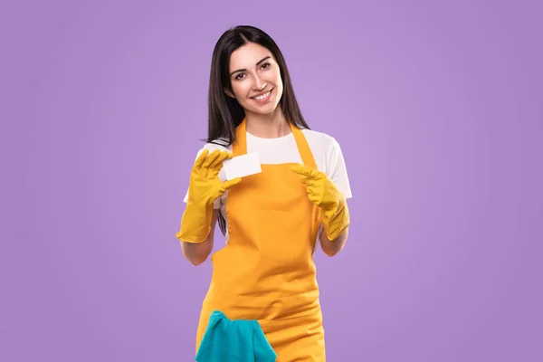Χαμογελαστή γυναίκα με ποδιά και γάντια που δείχνει λευκή επαγγελματική κάρτα — Φωτογραφία Αρχείου