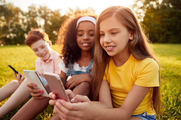 Multiraciale kinderen met behulp van gadgets in park — Stockfoto