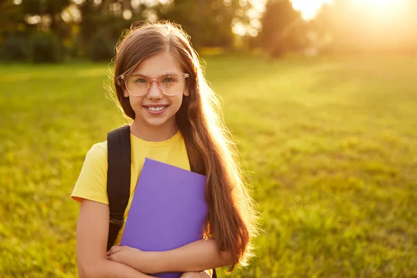 Joyeux écolière dans des lunettes debout dans le parc vert — Photo