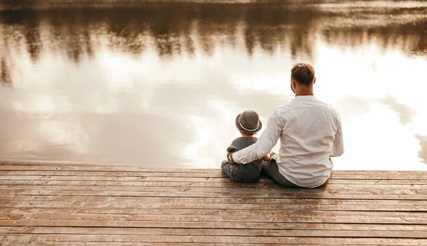 Père et enfant assis sur une jetée en bois près de la rivière — Photo