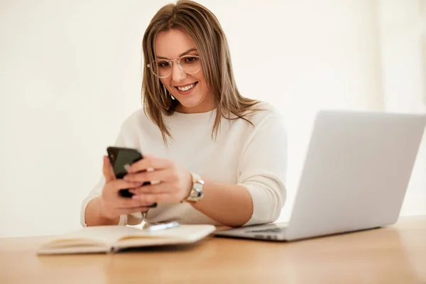 Blogueiro feminino alegre com laptop usando smartphone no café — Fotografia de Stock