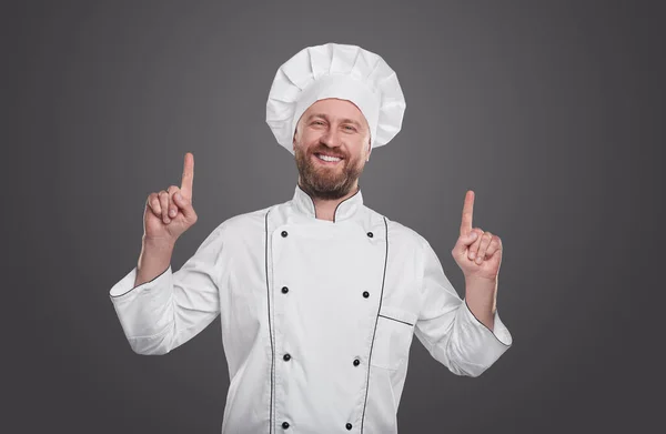 Chef alegre de uniforme apontando para cima — Fotografia de Stock