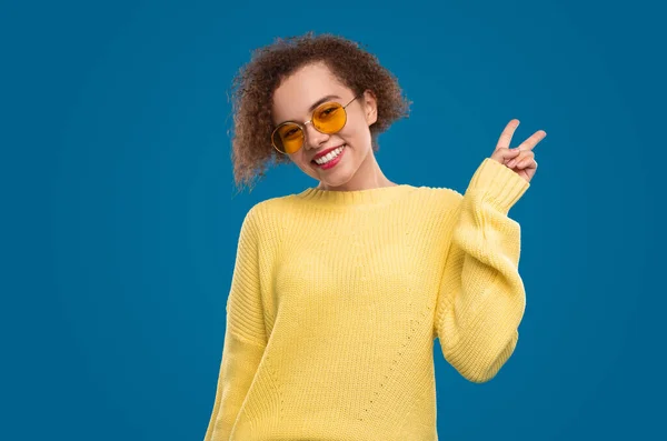 Весела молода жінка в жовтому светрі показує знак миру — стокове фото