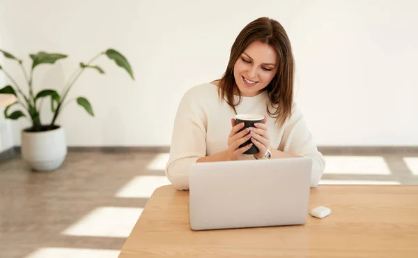 Femme souriante avec café et ordinateur portable sur le lieu de travail — Photo