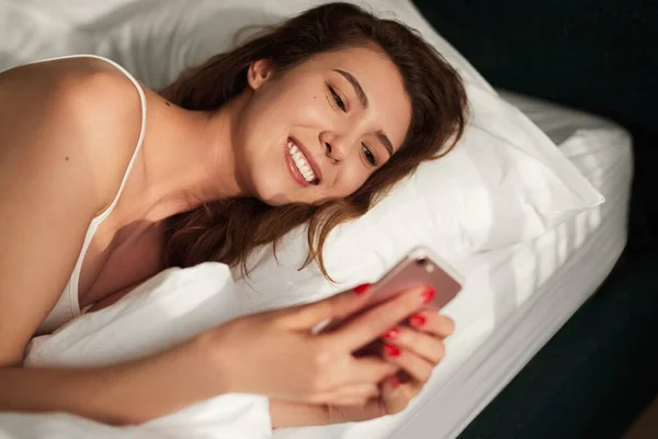 Giovane donna utilizzando smartphone a letto — Foto Stock