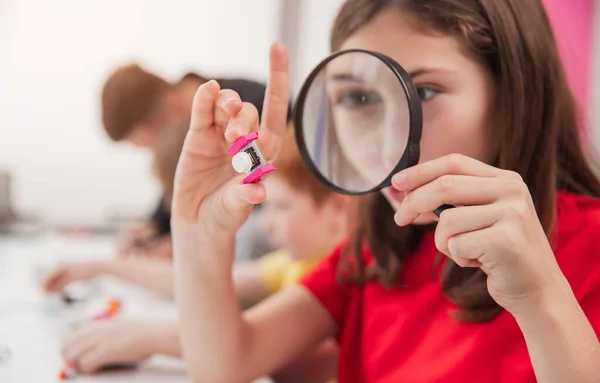 Girl with magnifier studying robotics in school