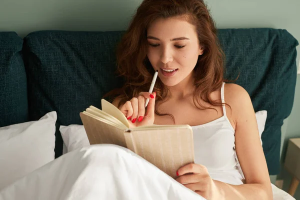 Yatağında günlüğü olan genç bir kadın.