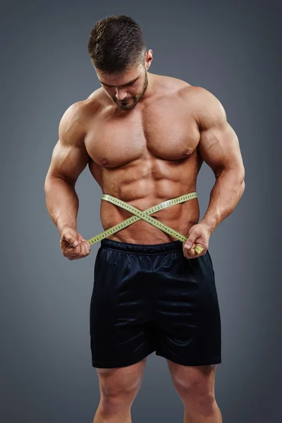 Bodybuilder measuring waist with tape measure — Stock Photo, Image