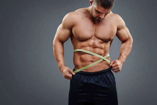 Bodybuilder measuring waist with tape measure