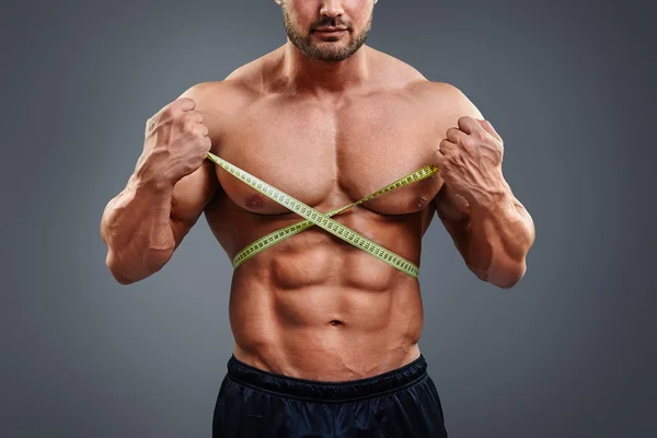 Bodybuilder measuring waist with tape measure — Stockfoto