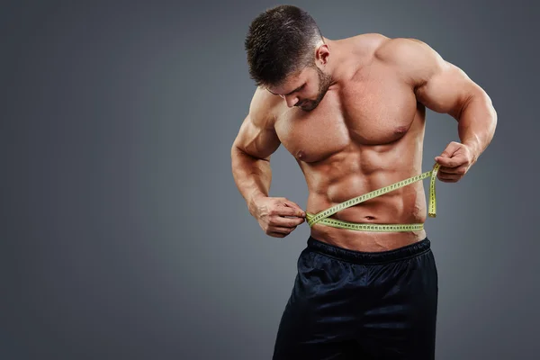 Bodybuilder measuring waist with tape measure — Stockfoto