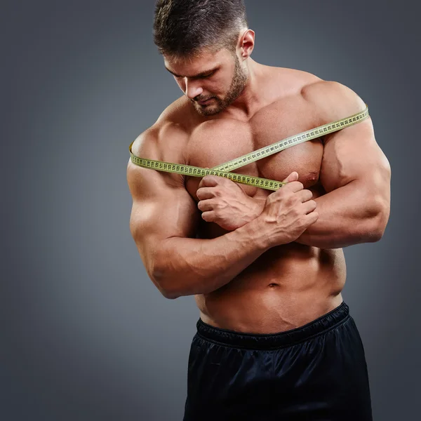 Bodybuilder measuring shoulders with tape measure — Stockfoto