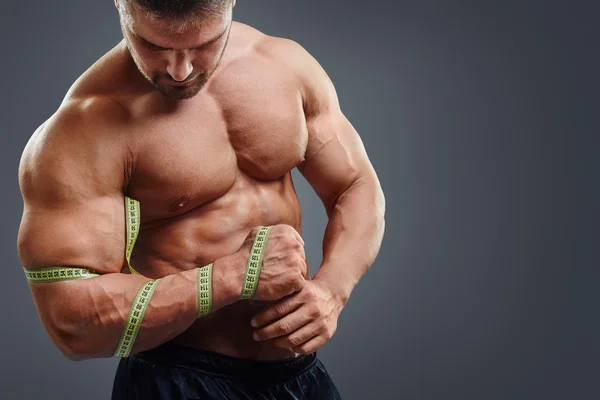 Bodybuilder measuring biceps with tape measure — Stock fotografie