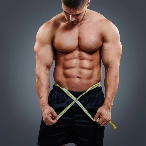 Bodybuilder measuring waist with tape measure — Stockfoto